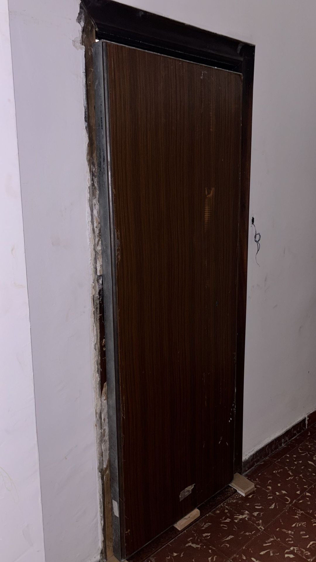 Puerta acorazada de color wengué en proceso de instalación con marco metálico en pared de obra